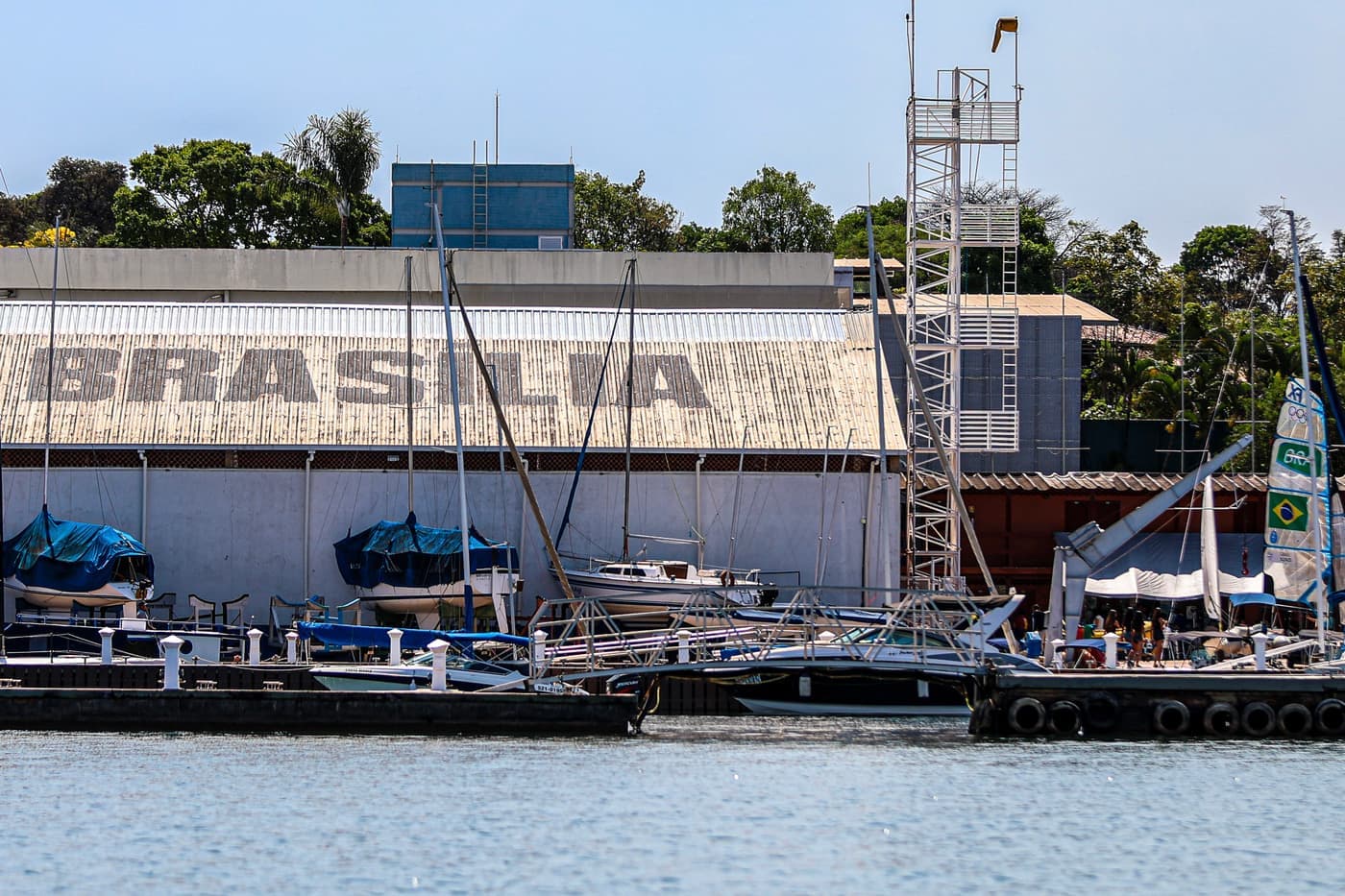 Galpão do Iate Clube de Brasília visto da água, com barcos atracados nos pontões em frente